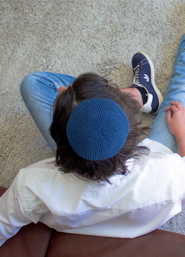 Penelope D handmade crochet kippah worn by a man sitting on a cream carpet
