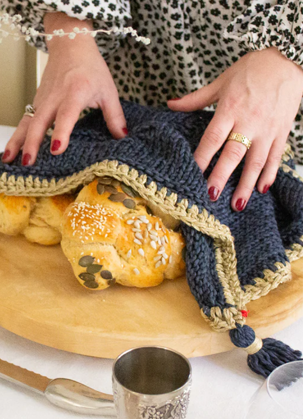 Woman blessing a challah beneath a navy Penelope D challah cover with gold edging